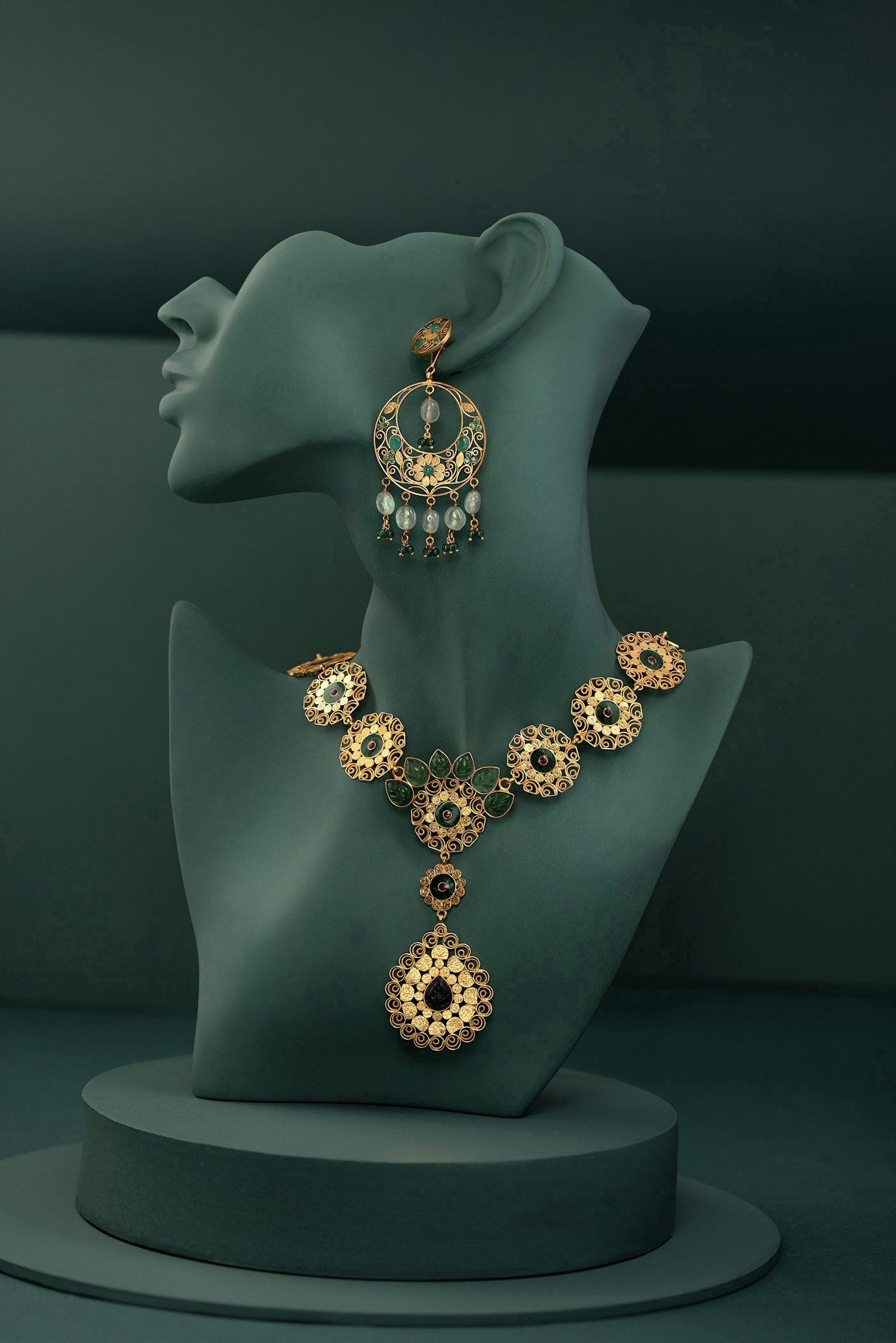 Traditional gold necklace and earring set displayed on dark green